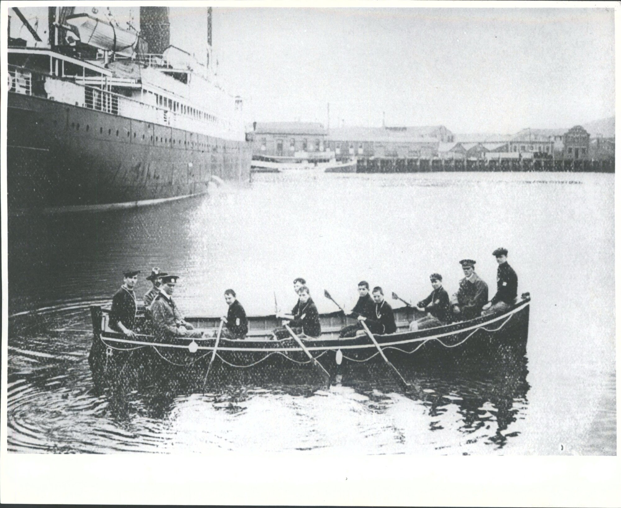 Caption: 'The Sea Scouts' new boat, "Foam Queen" at the Dunedin Wharf. The boat carries of sea scouts in the Dominion. Seamanship instructor, H. R. Cole (in the stern) with District Commander Jones and Scoutmaster M'Pherson [? in the bow]