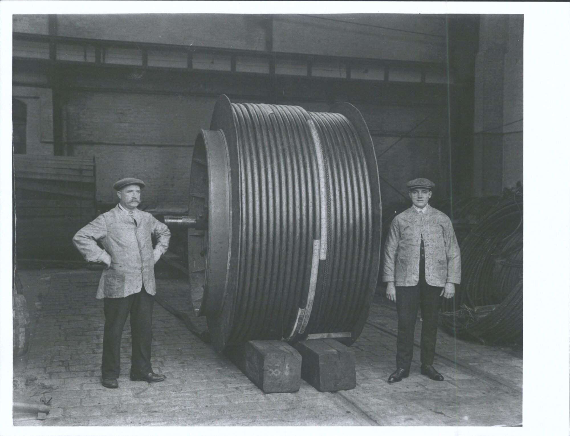 Men standing next to large spindle of cable