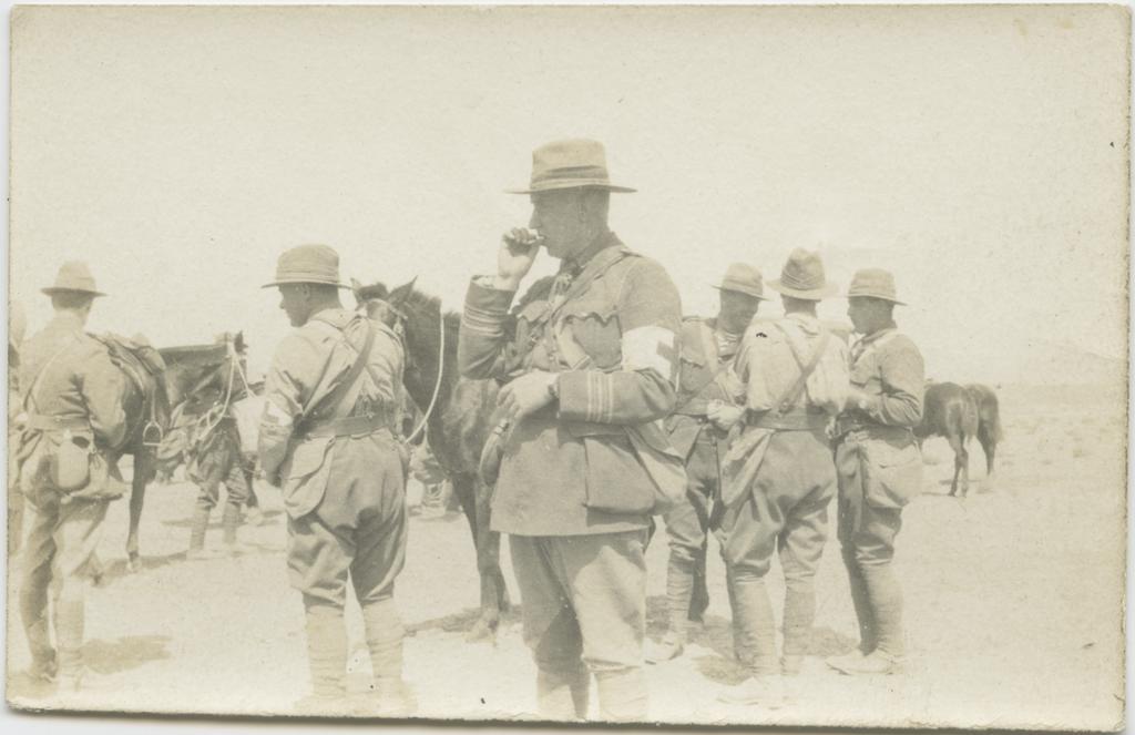 A group of soldiers, at least two with red cross arm bands, standing next to horses
