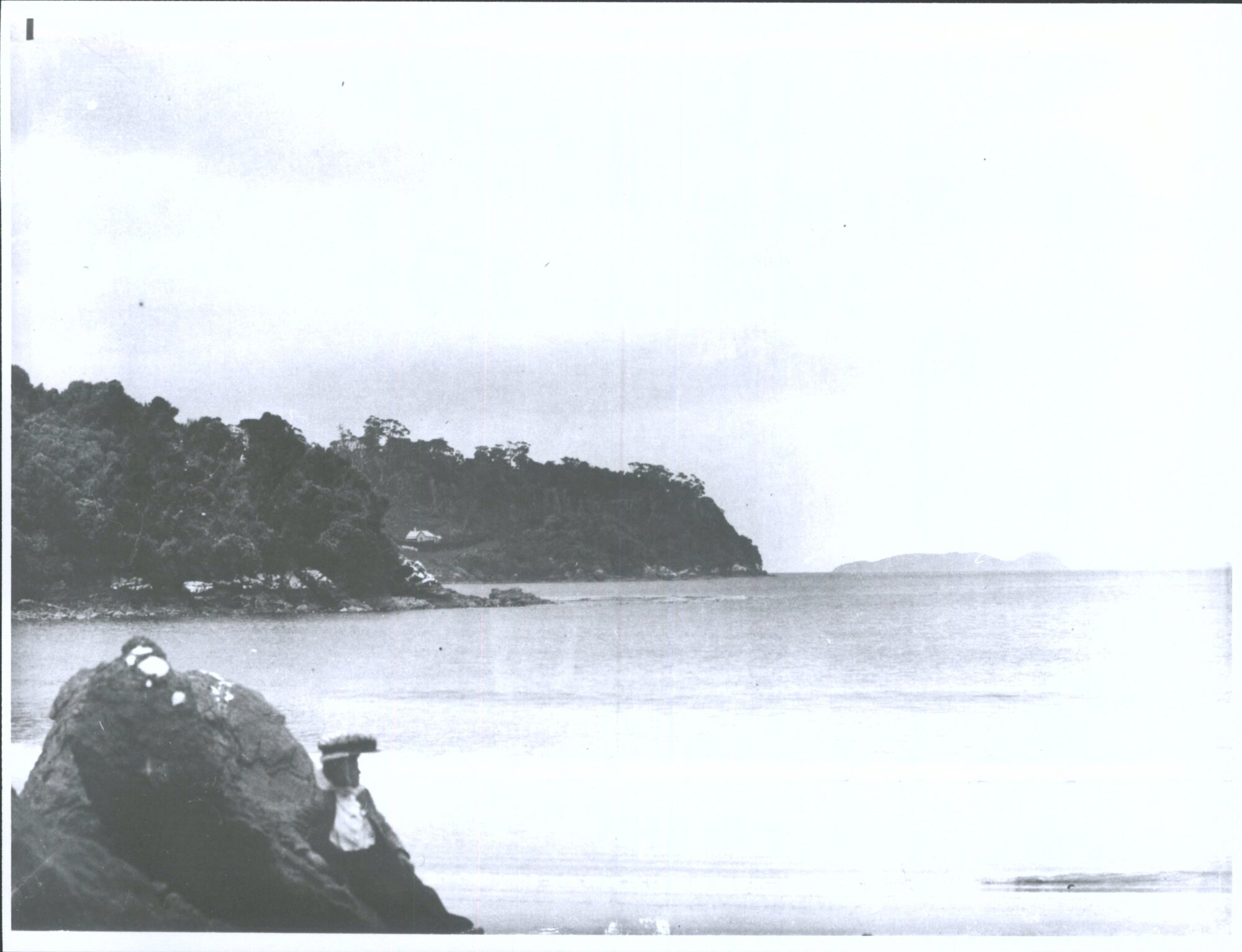 A woman gazes out from a rock on a beach