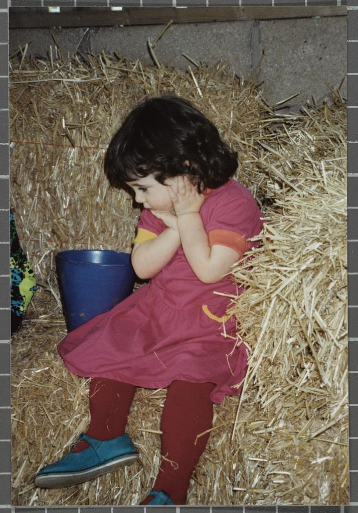 Young girl sitting on a hay bale, next to a bucket