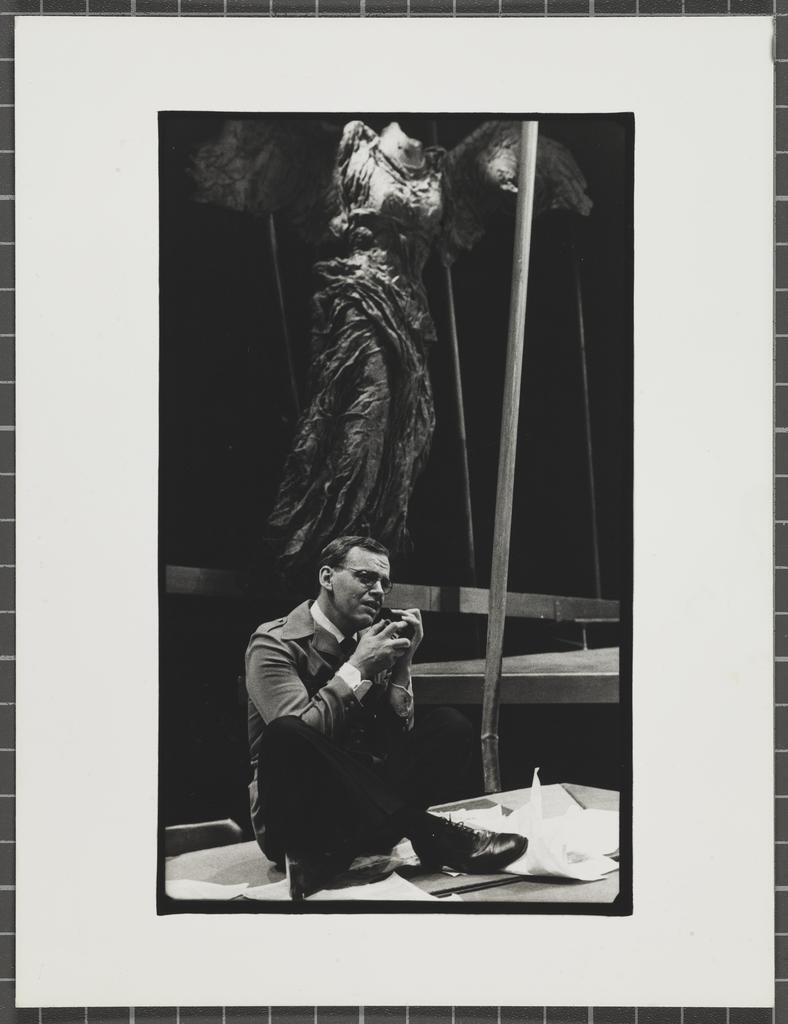 Man with glasses sitting cross-legged under angel figure, Downstage Theatre production of 'Heroes and butterflies'