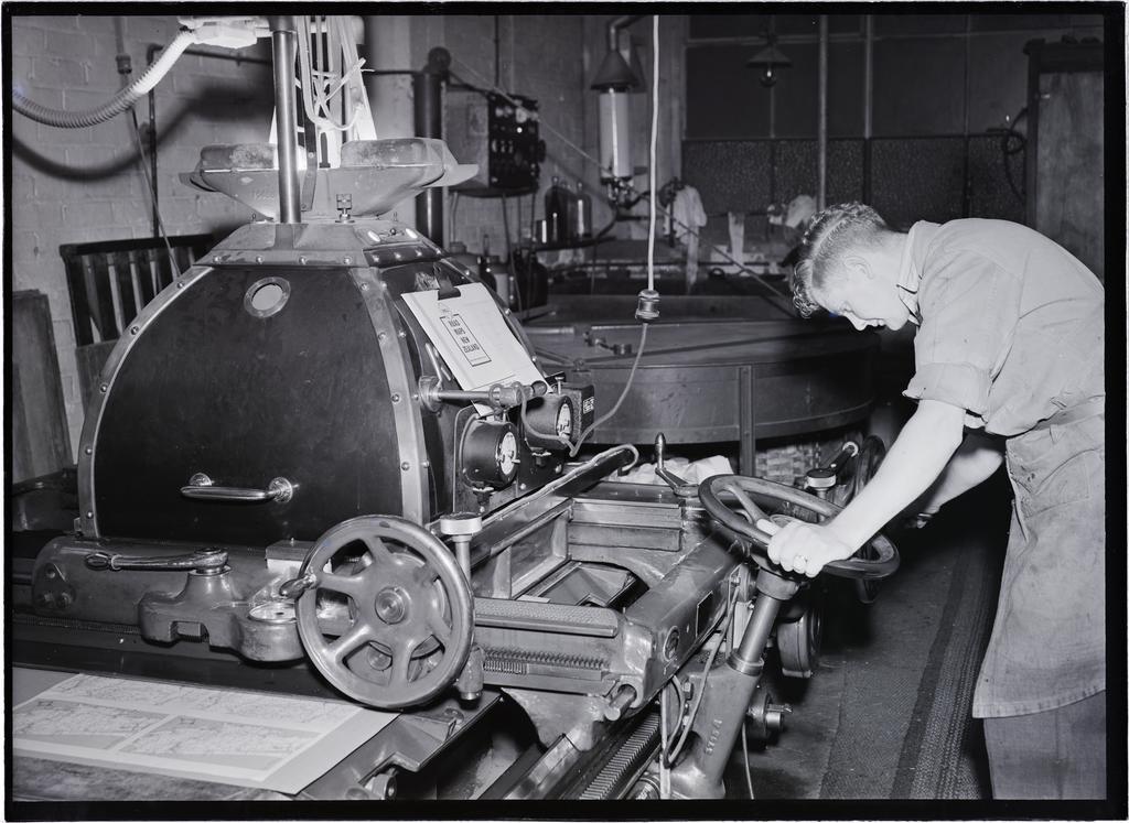 A young man at a machine, in the process of printing a 'Shell Road Maps New Zealand' book, Coulls Somerville Wilkie, Crawford Street, Dunedin