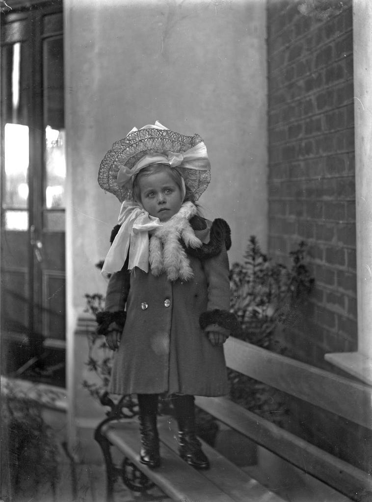 Em standing on garden seat wearing hat and coat