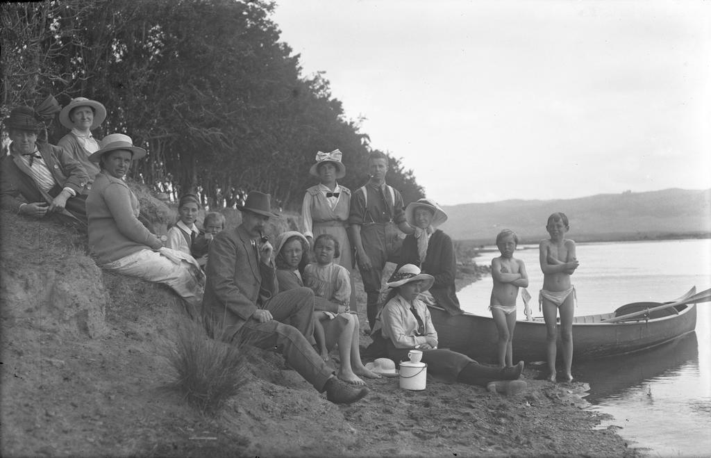 McGeorge family group of adults and children on the shore with a canoe, Karitane