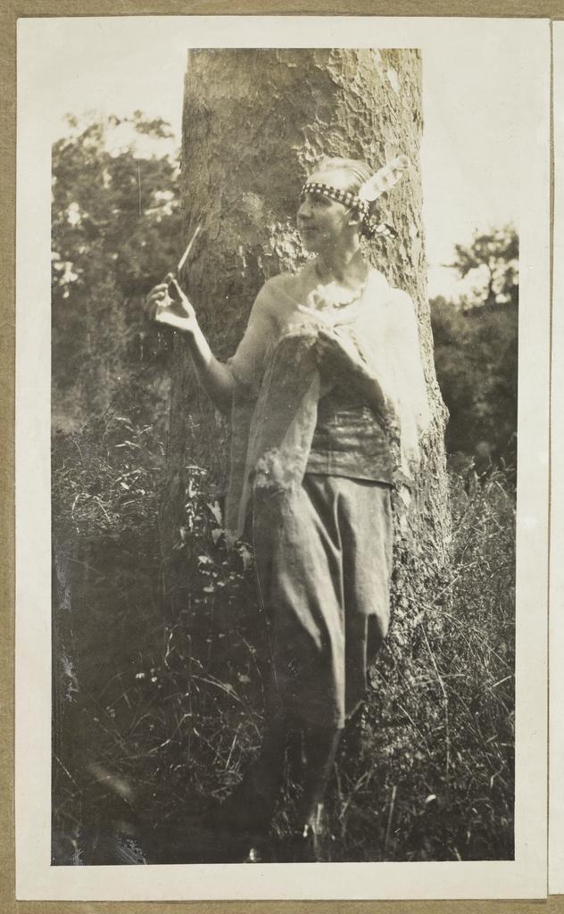 James Courage in drag, standing against a tree