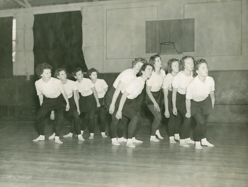 Ten dancers, leaning over, looking right