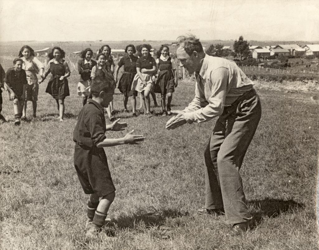 Smithells playing with boy, while group of girls watch in background.