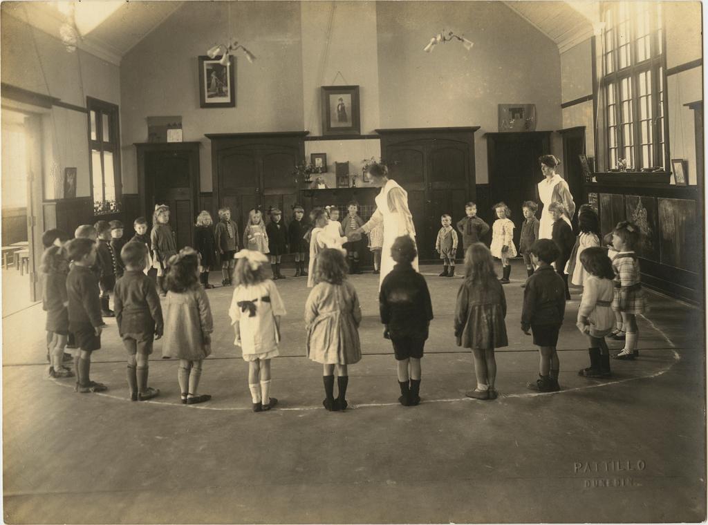 Children standing in circular formation, with two women in uniform