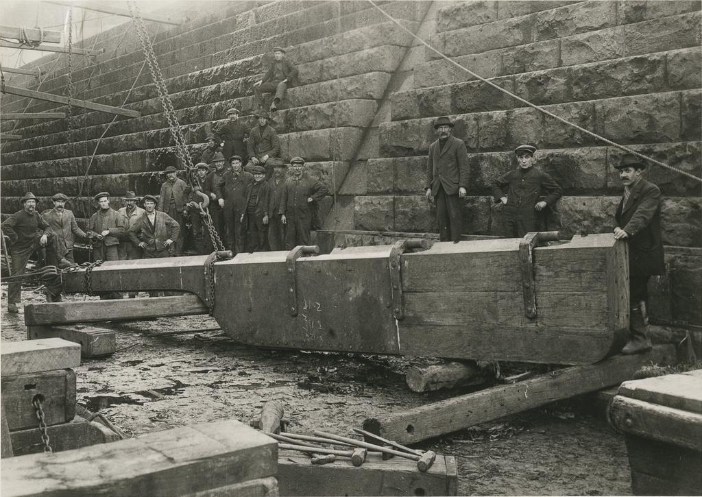 Group of men standing beside large rudder