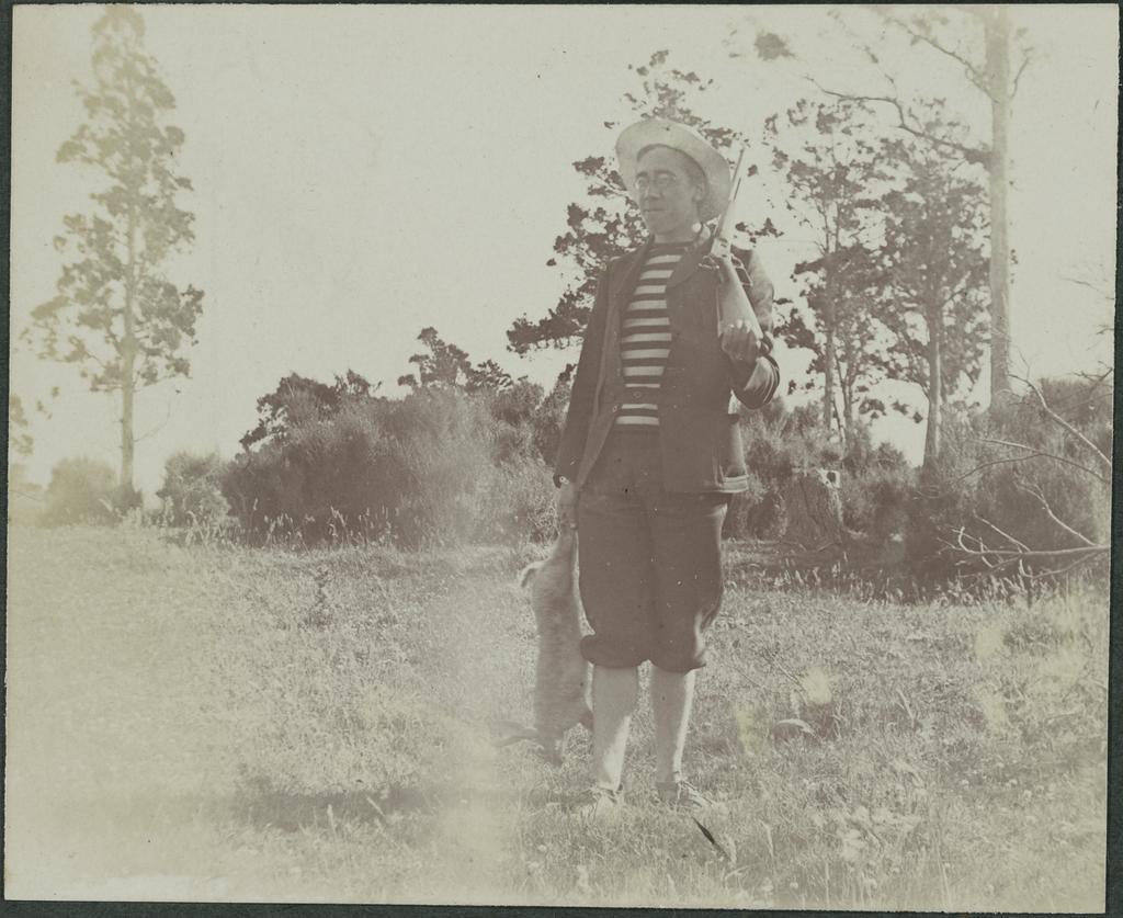 W.A. Curzon-Siggers carrying rifle and holding dead rabbit