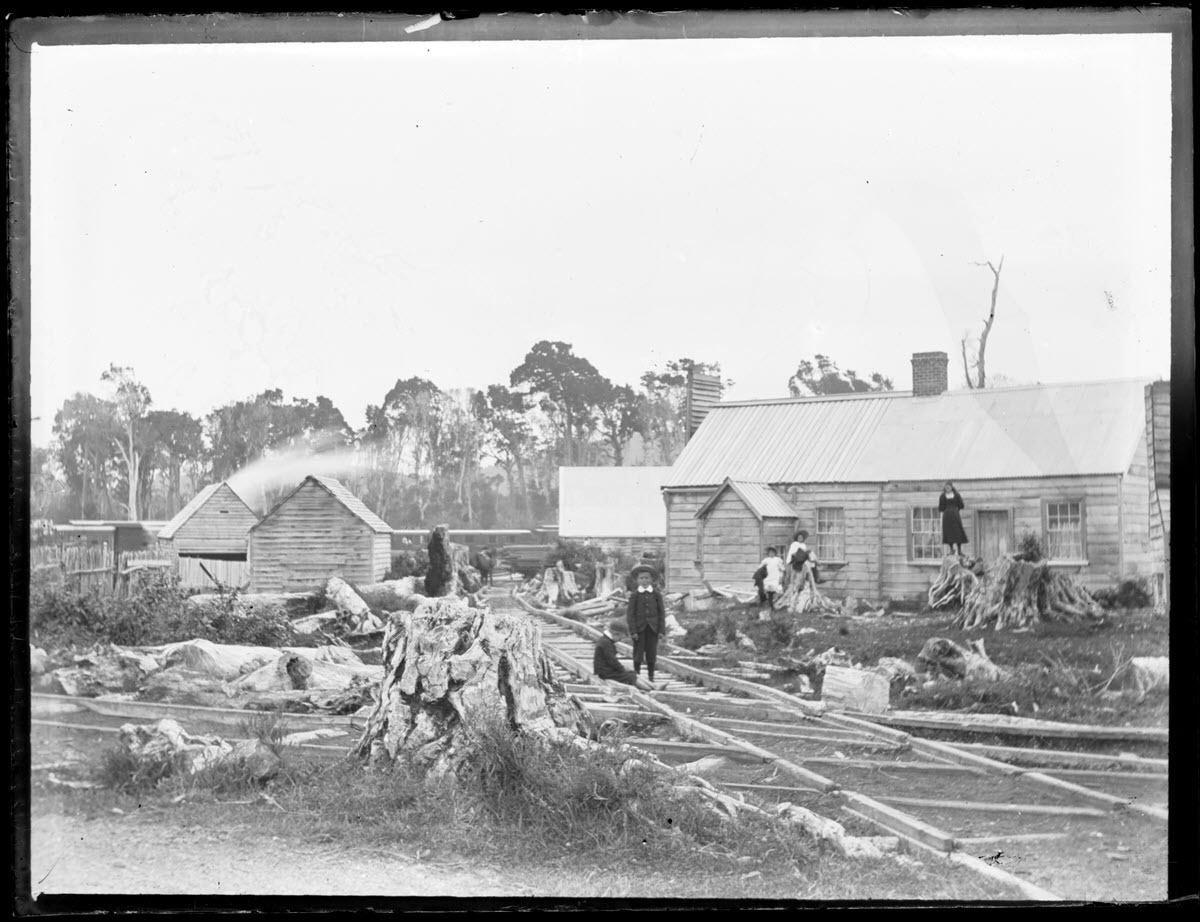 Scene showing railway, wooden buildings, children, and cleared land