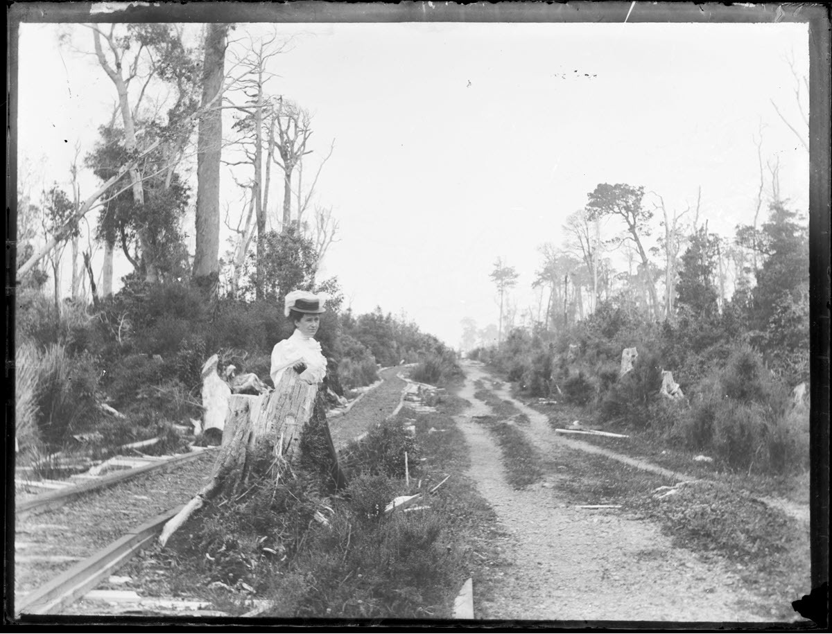 Scene at Invercargill [?], showing a road, timber tramway tracks, and a woman