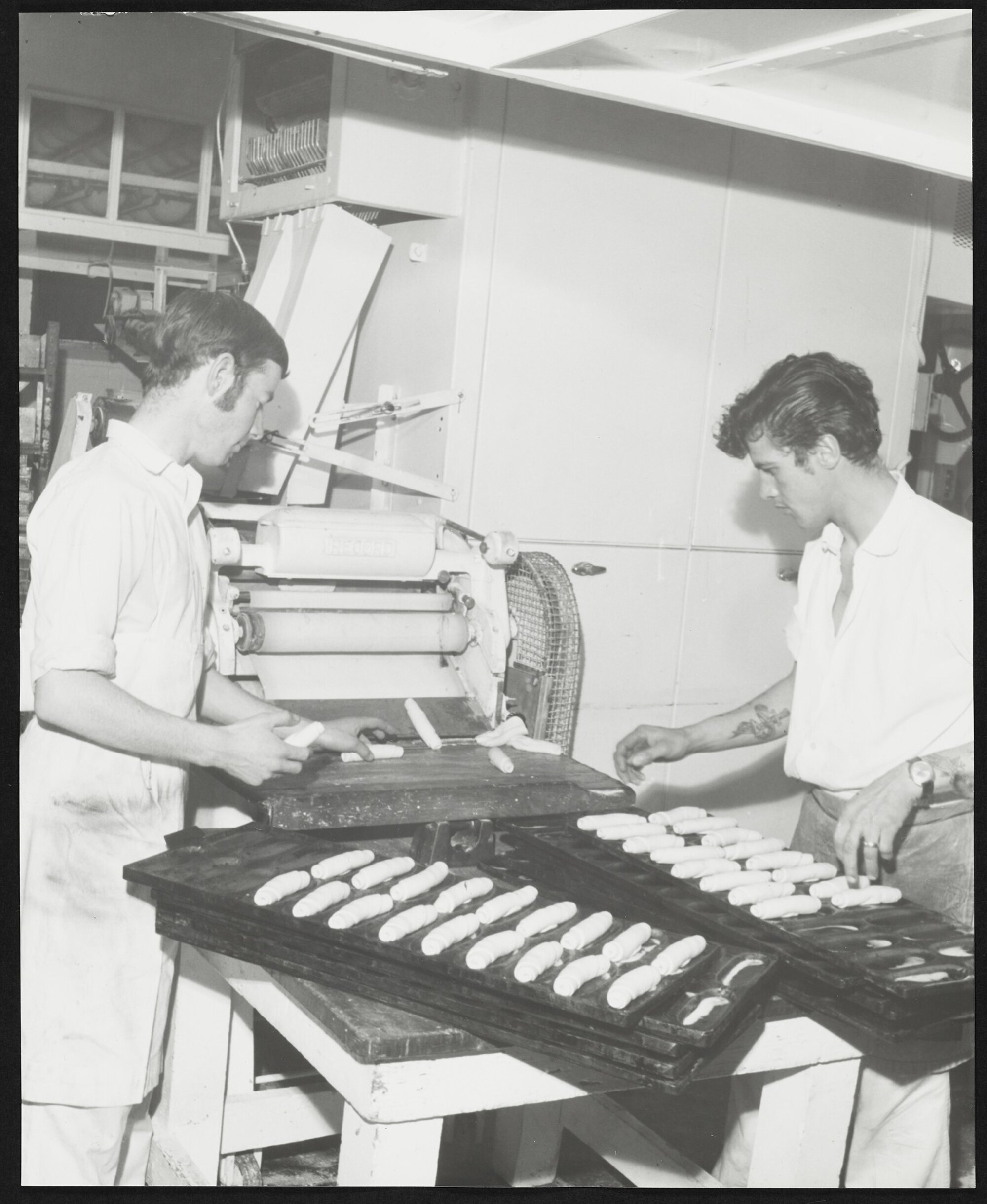 Two men at machine turning out rolled pastry in Laurenson's Bakery 