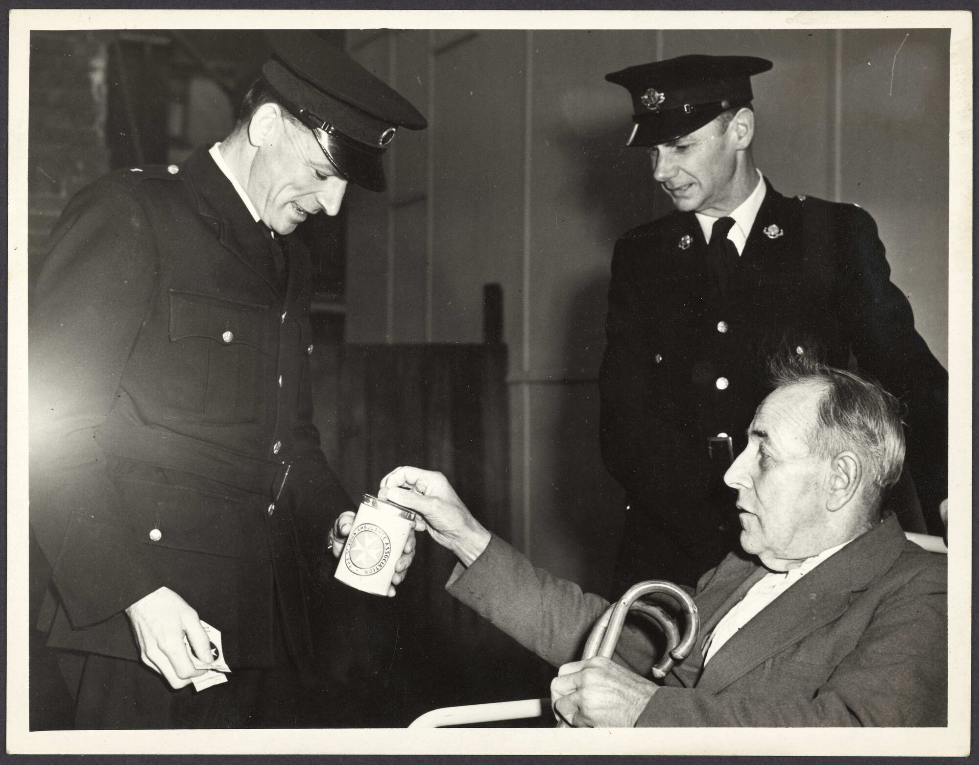 'Mr T.J. Moynihan, a patient of Parkside Hospital, handing a donation to Ambulance Drivers Messrs. M.V. Jane and J.R. Wilson when he arrived at the School of Physiotherapy'