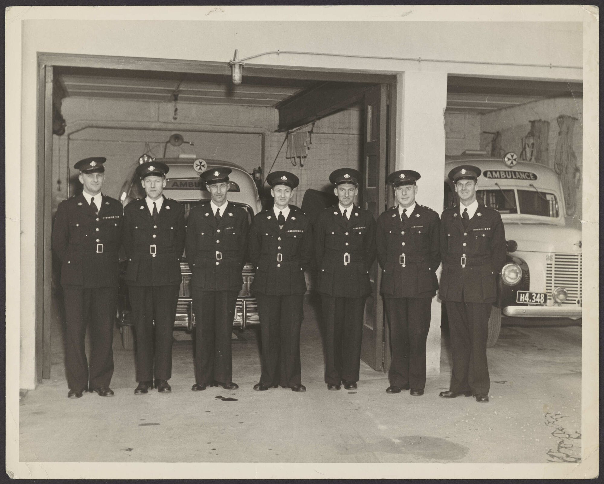 Seven men in St John uniform, with two ambulances behind