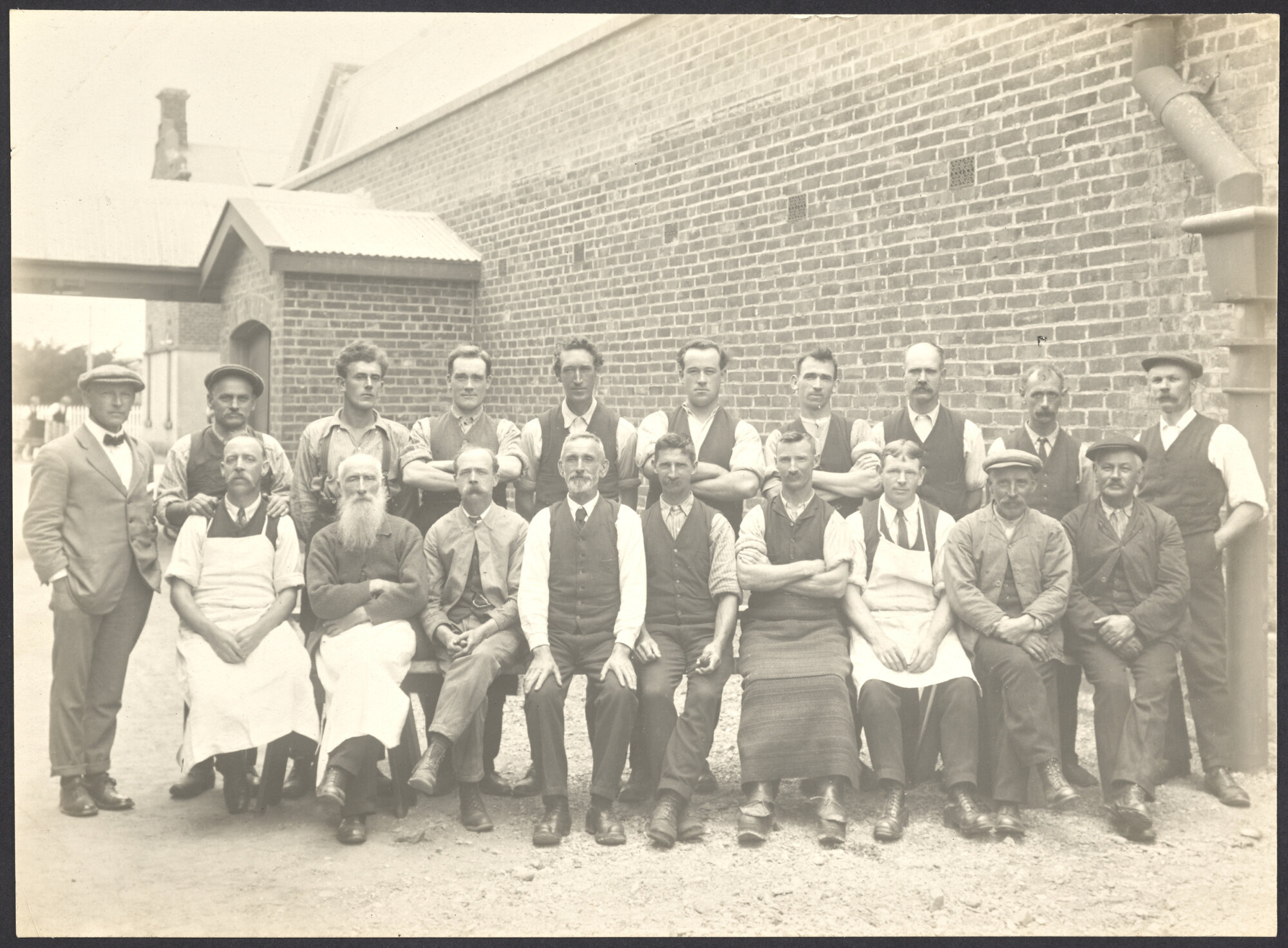 Group of male workers seated in front of brick building