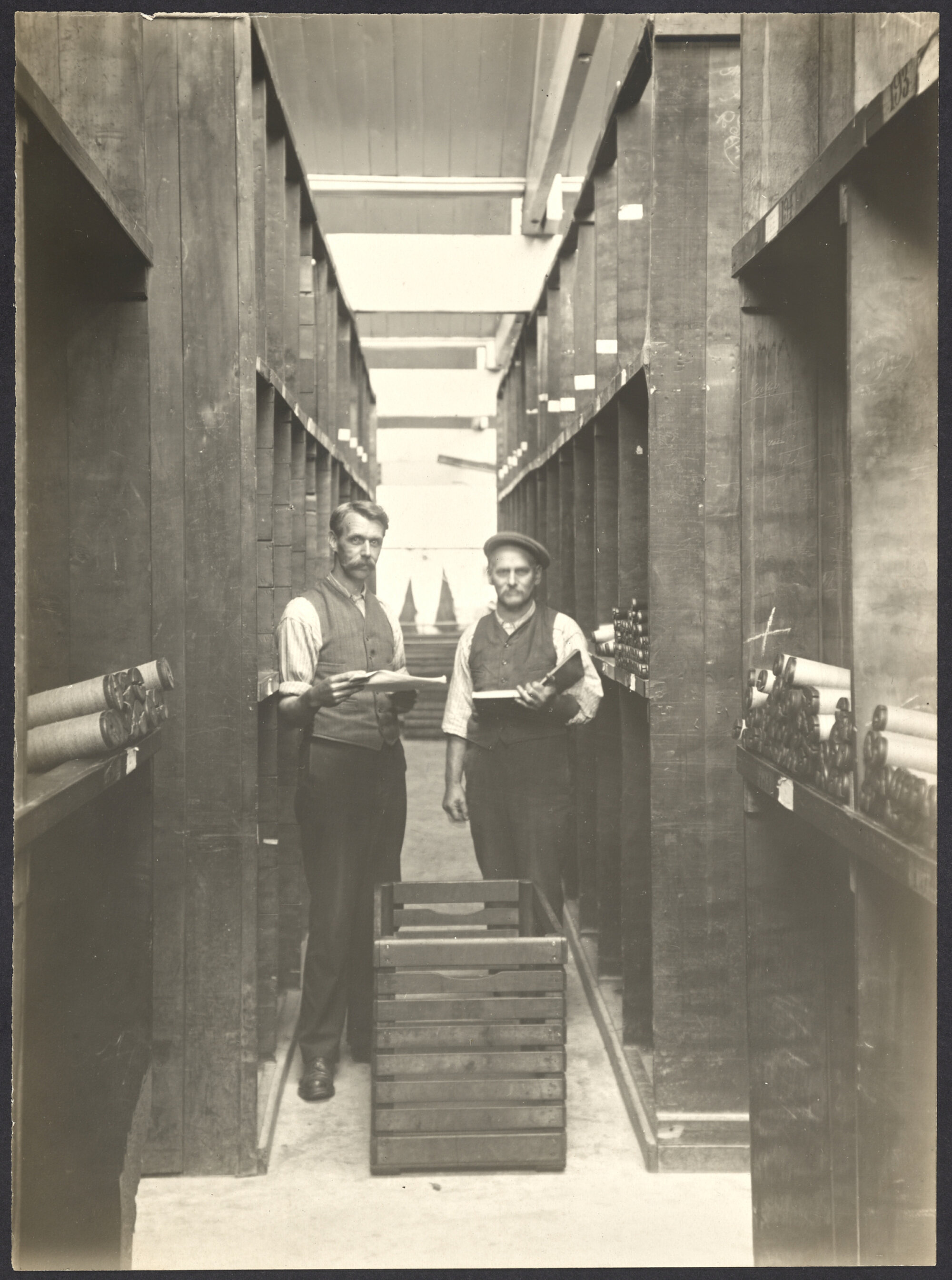 Two men in storage area with bobbins of yarn