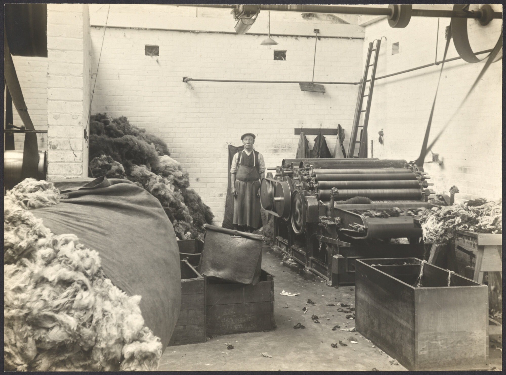 Worker with carding machine and piles of uncarded wool