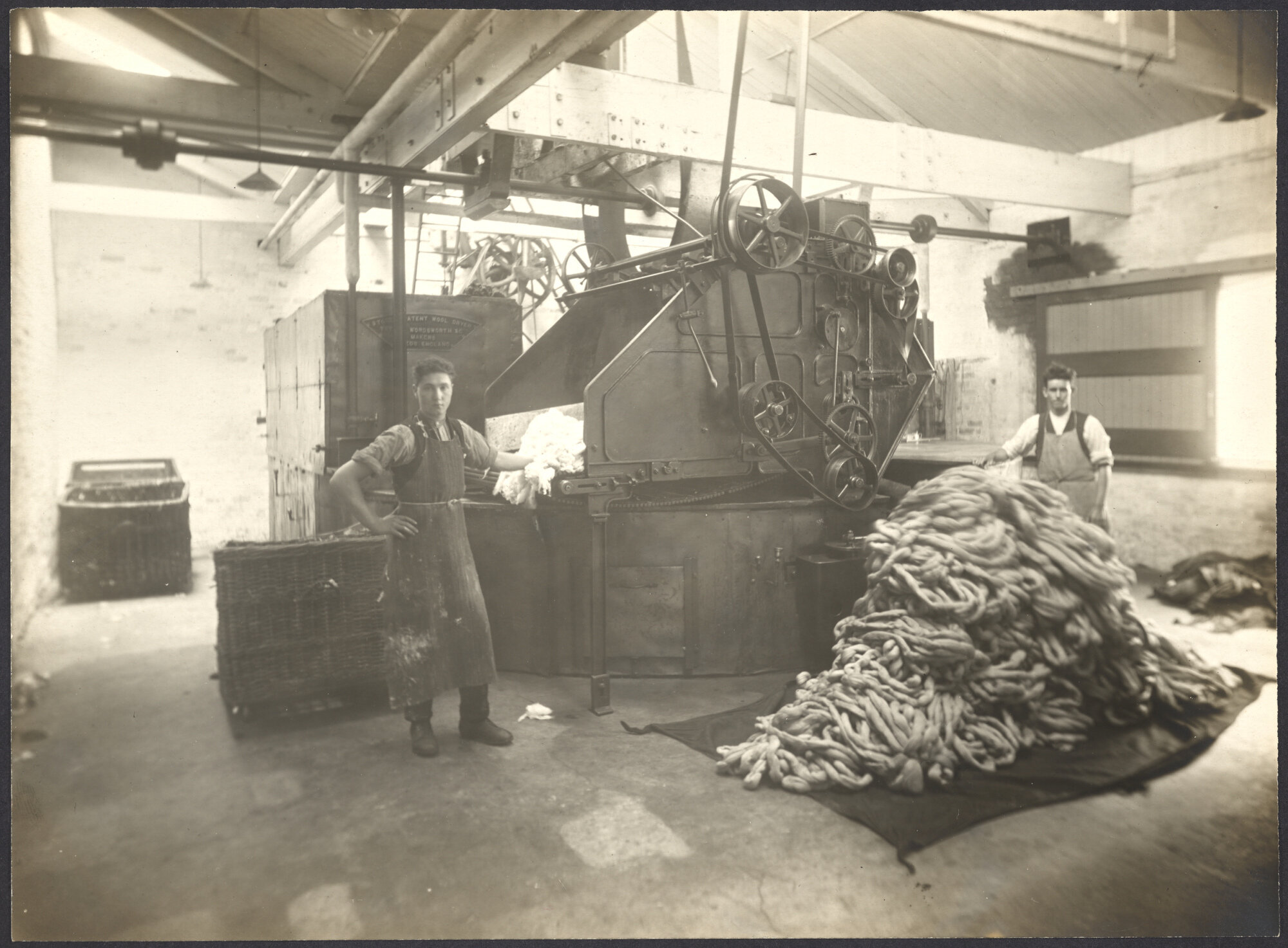 Two workers and machinery, wool being carded into roving