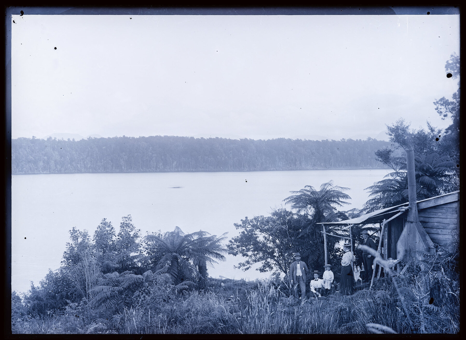 Five people outside a hut on a riverbank, Westland