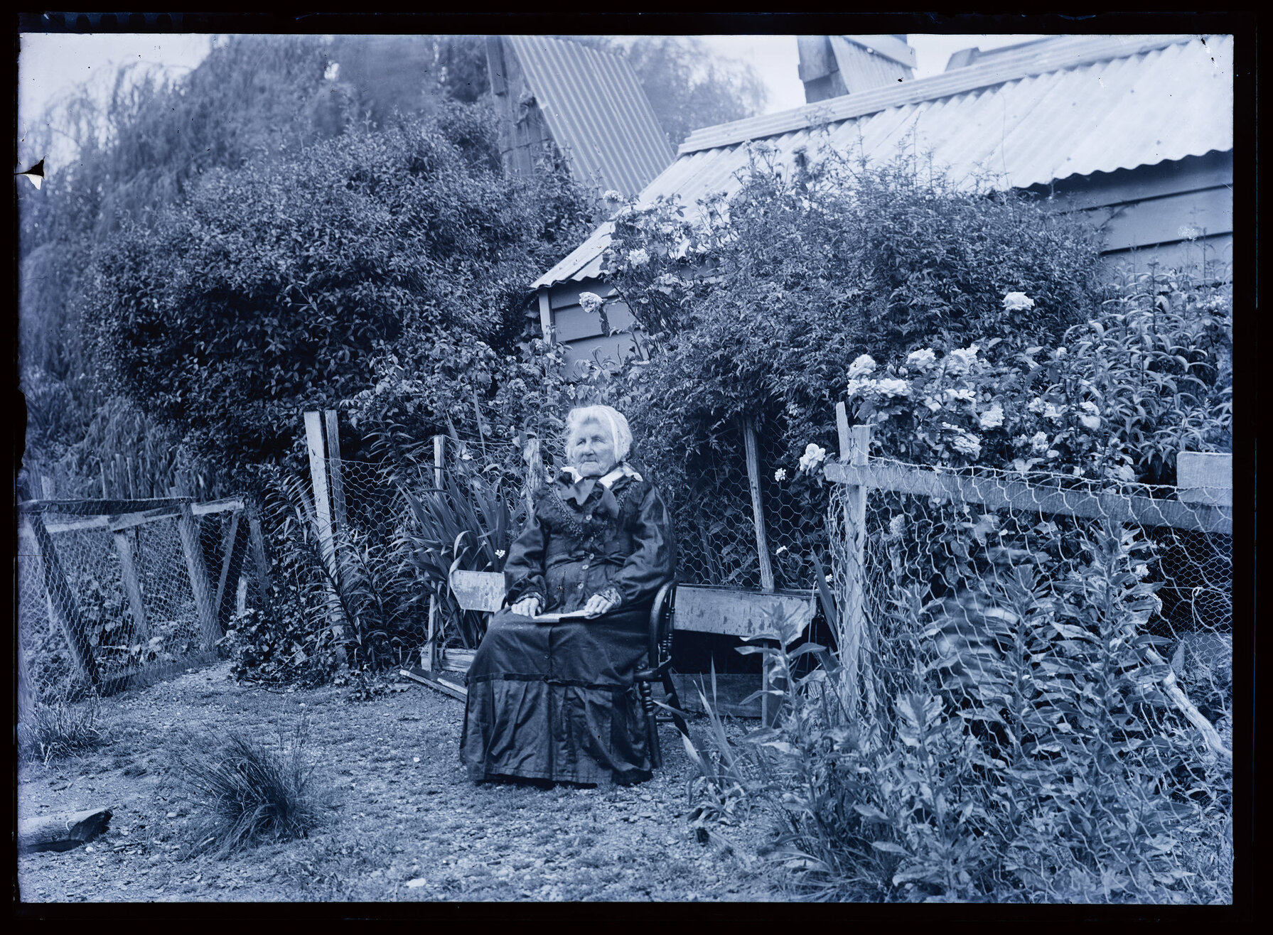 Older woman seated on a chair in the garden of a farmhouse