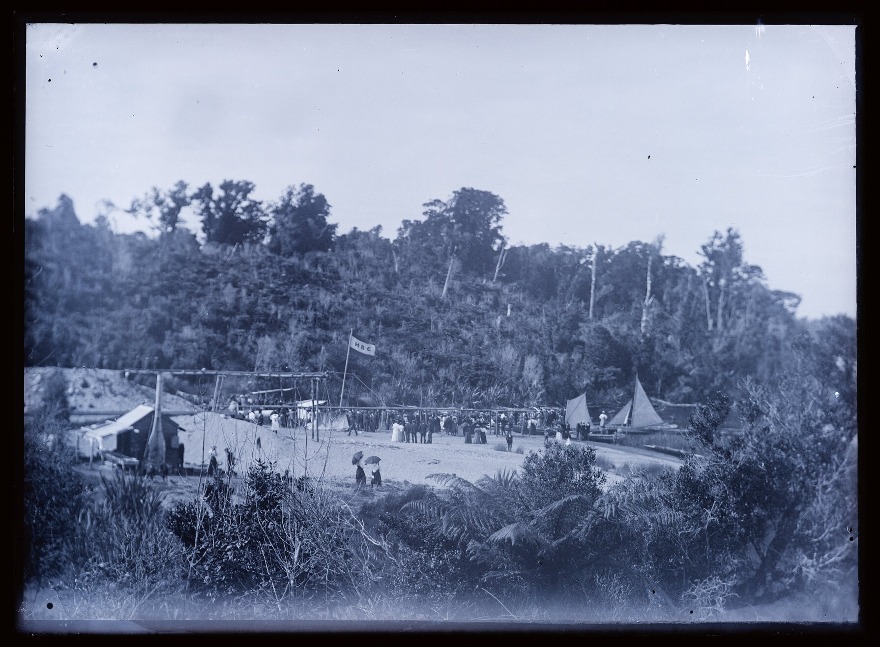 Large group on a beach at an event, Hokitika Boating Club flag visible
