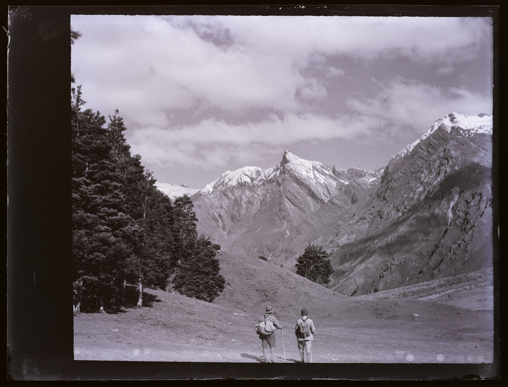 Two people standing in the valley of the East Matukituki, looking towards Sharks Tooth Peak