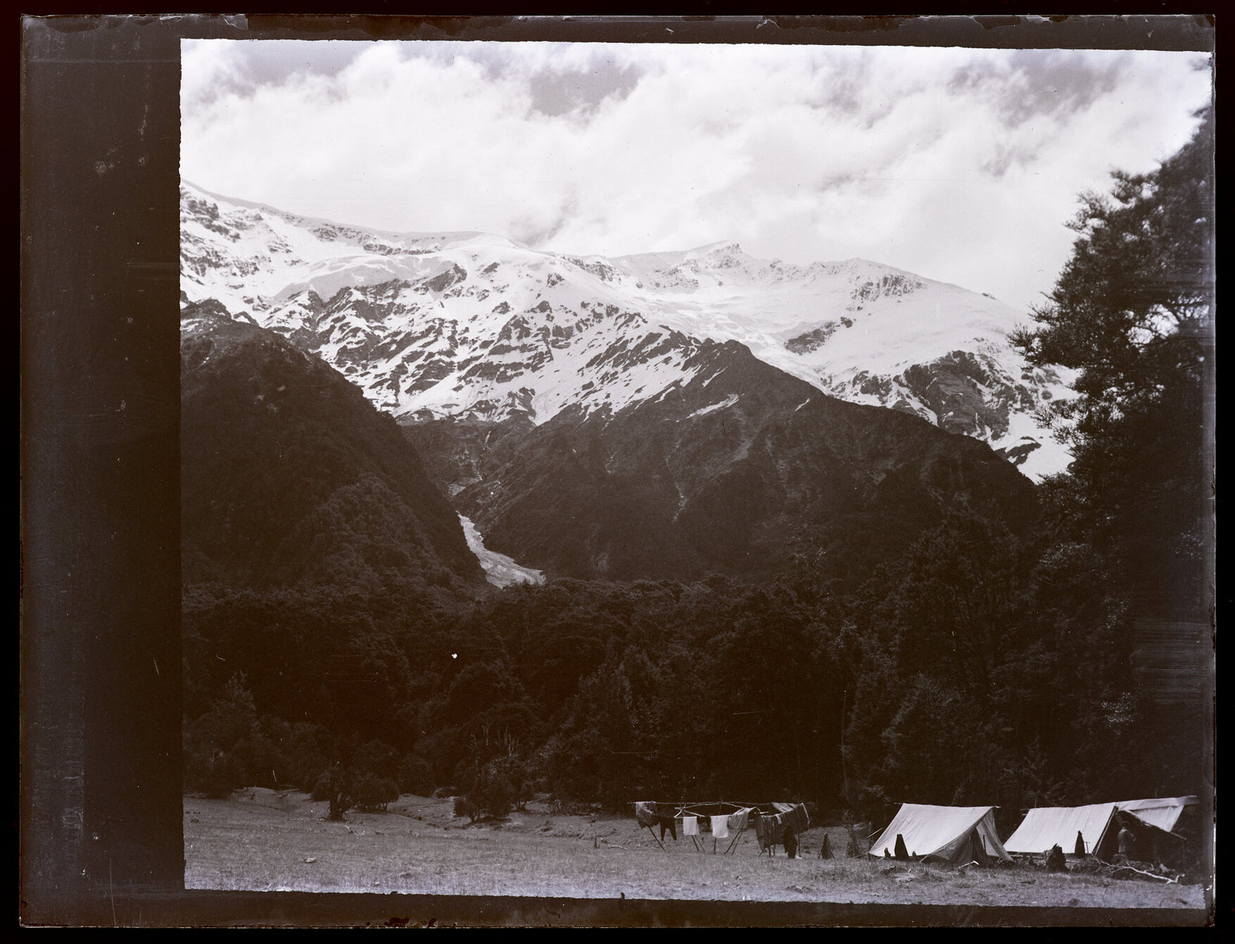 Unidentified snowy peaks with camp below, with large circular drying frame for laundry