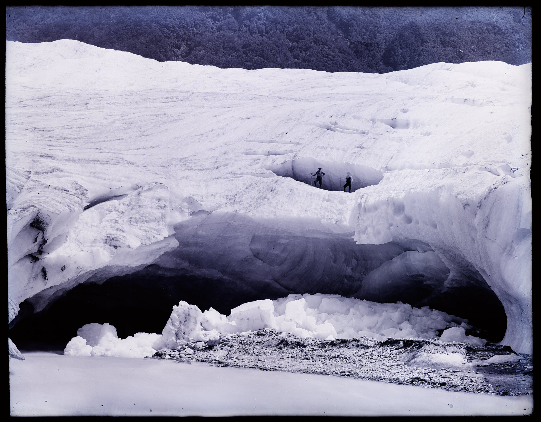Two people standing on an arch of glacial ice next to a stream, Westland