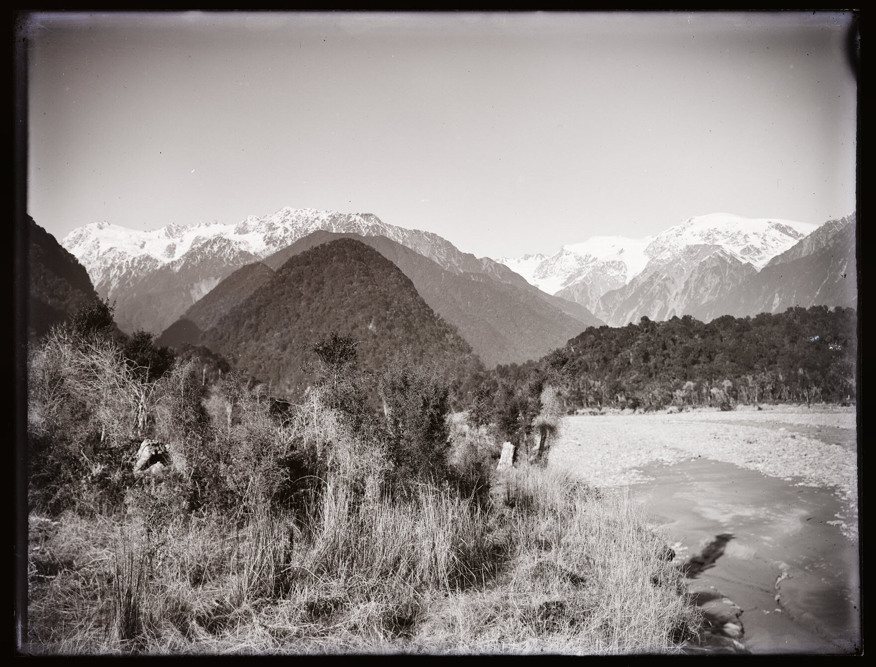 View from riverbank towards mountains and Franz Josef Glacier