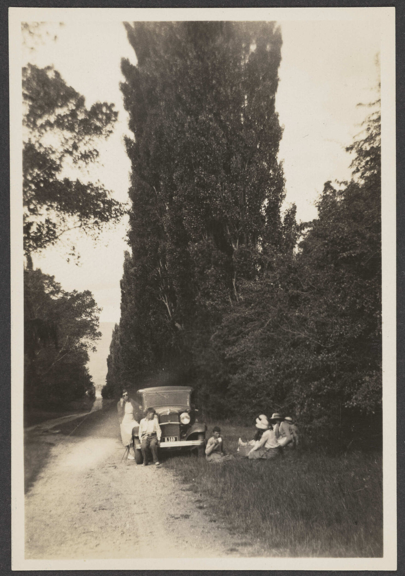 Group of people sitting by car parked on gravel road