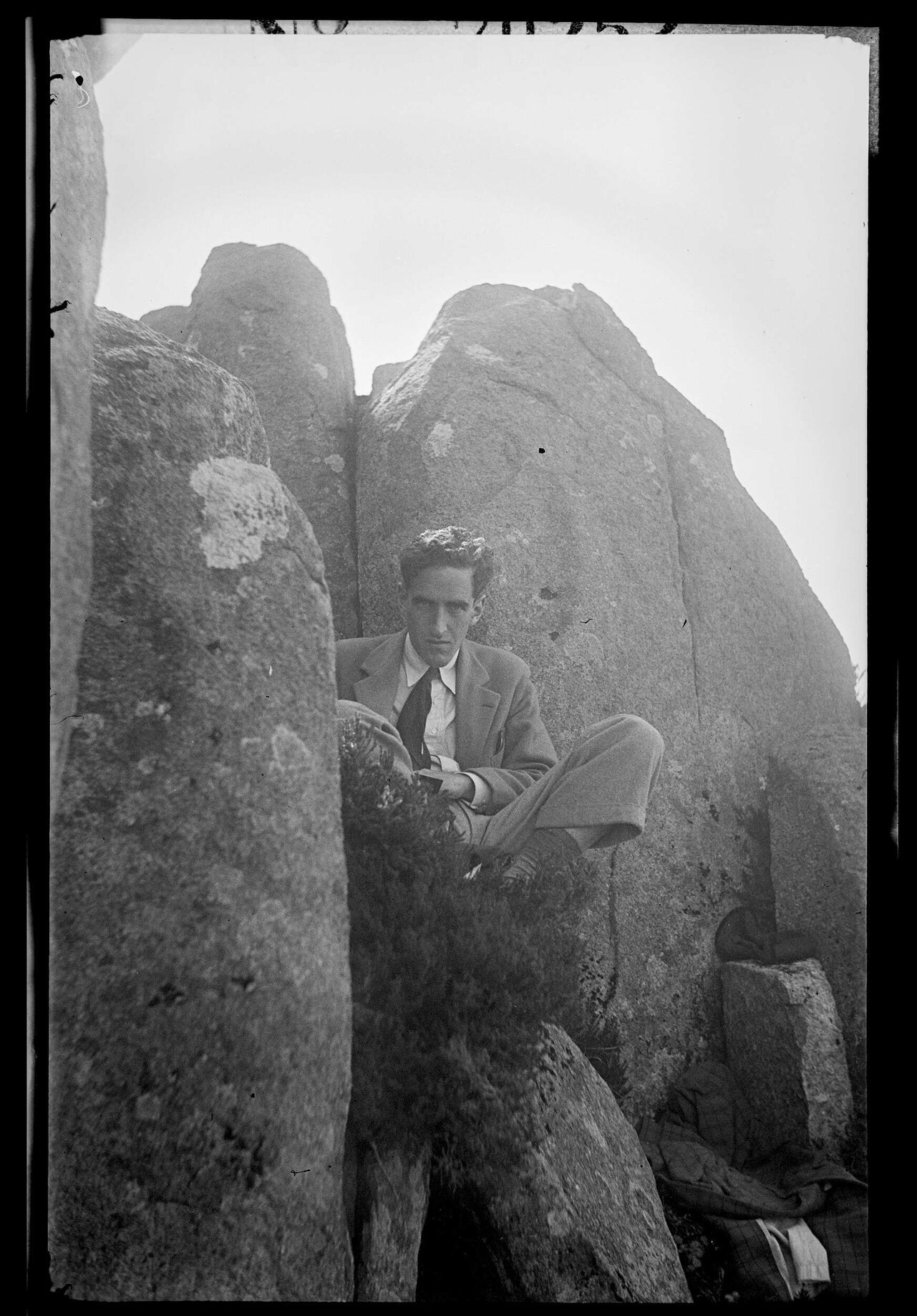 Charles Brasch sitting between large rocks