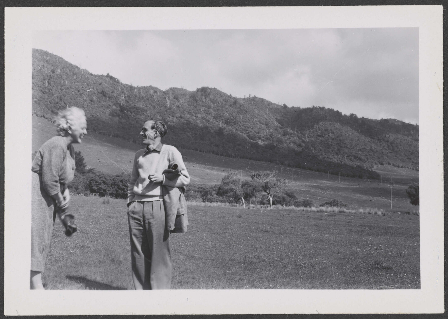Charles Brasch and a woman in a paddock with hills in the background