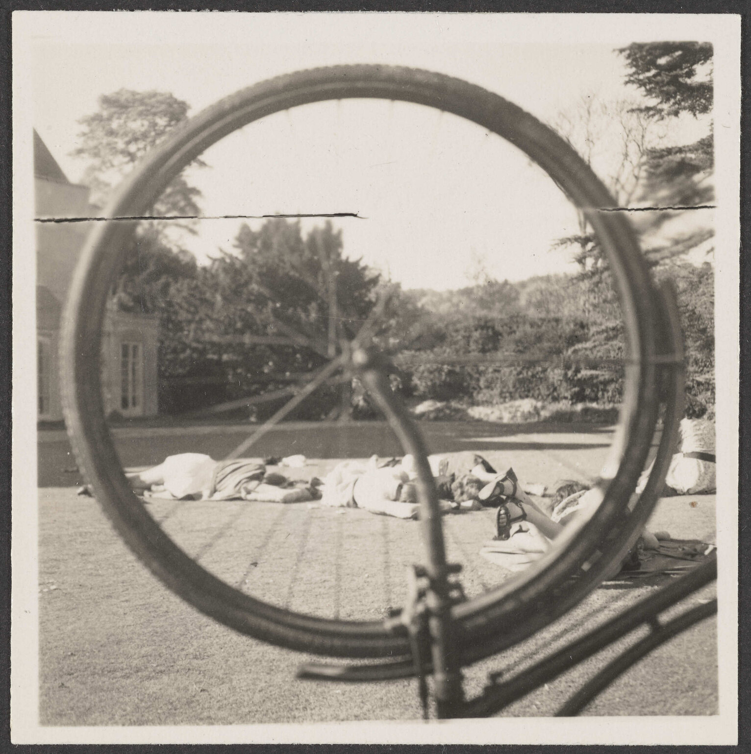 Photograph taken through bicycle wheel of people lying on a lawn