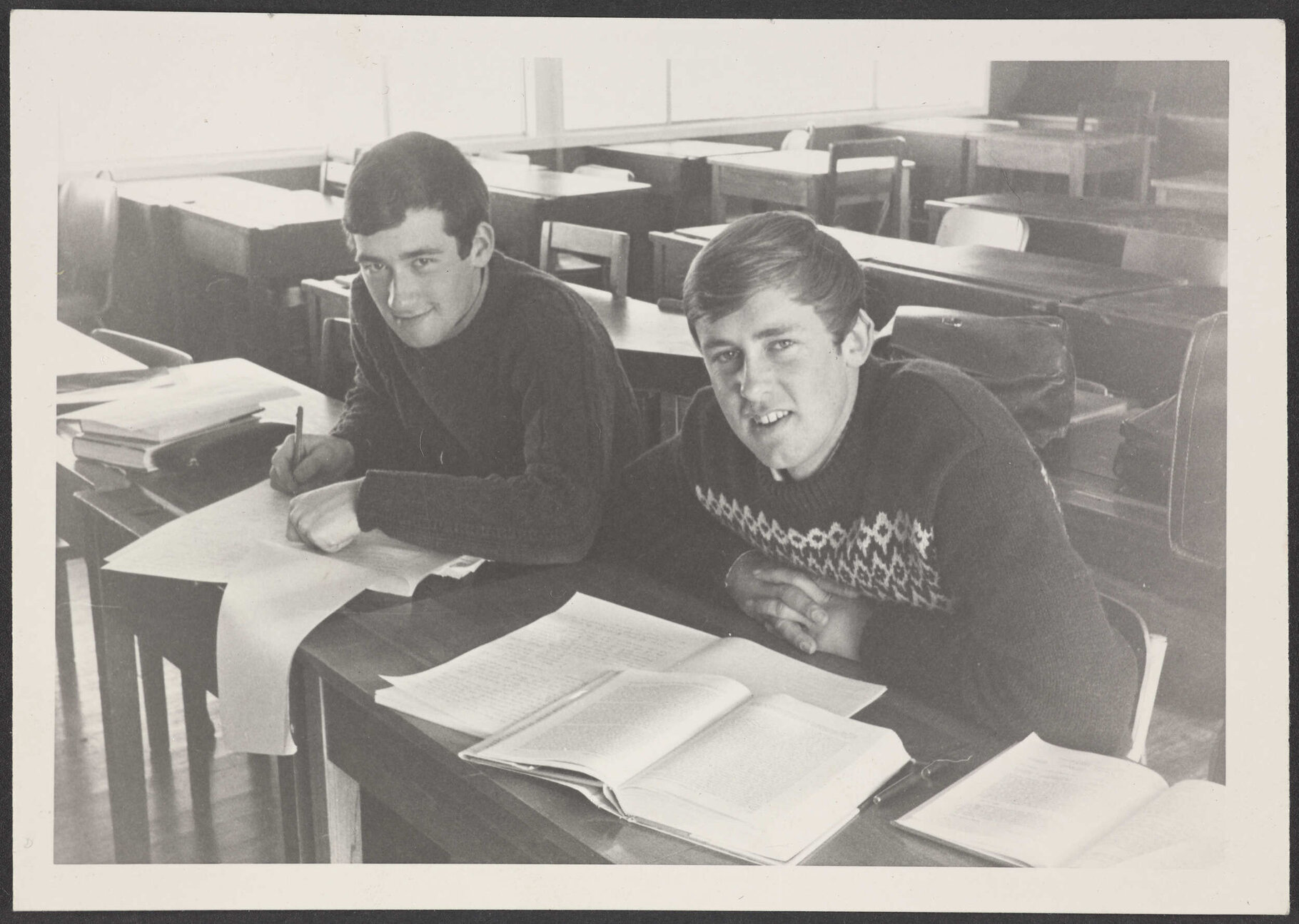 Two young men sitting at desks, with books and notes