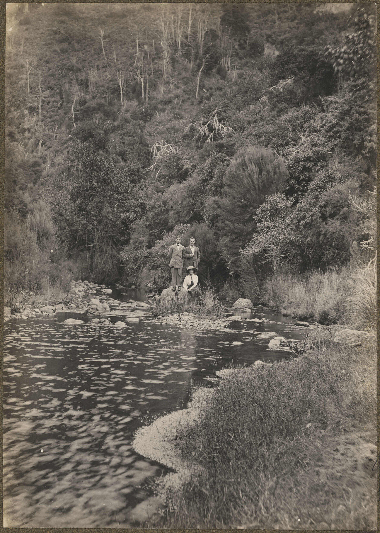 Two unidentified men and one unidentified woman on a boulder in the middle of a river