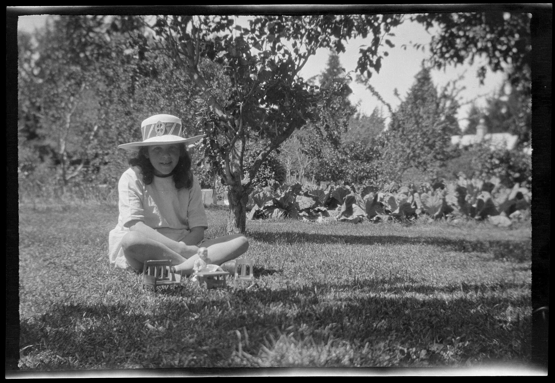 Girl sitting cross-legged on grass, with miniature doll and furniture