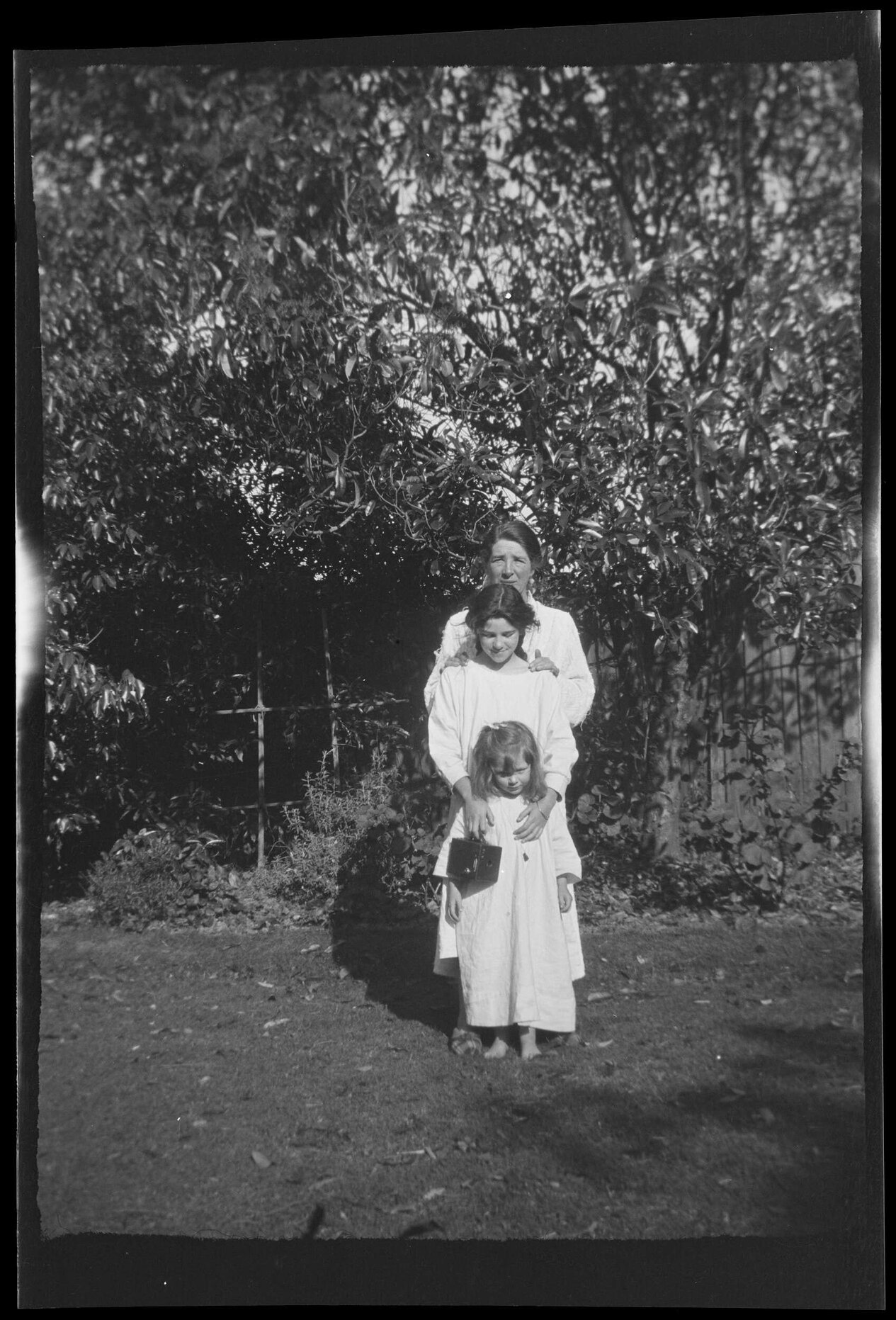 Emily Forsyth with two girls wearing smocks, standing in a garden