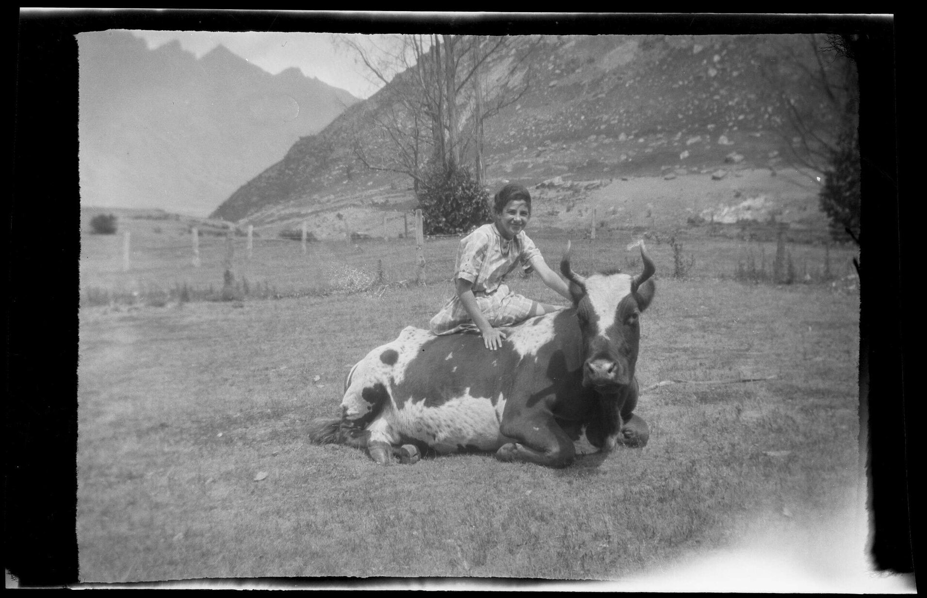 Girl sitting on a cattle beast, with mountains in the background