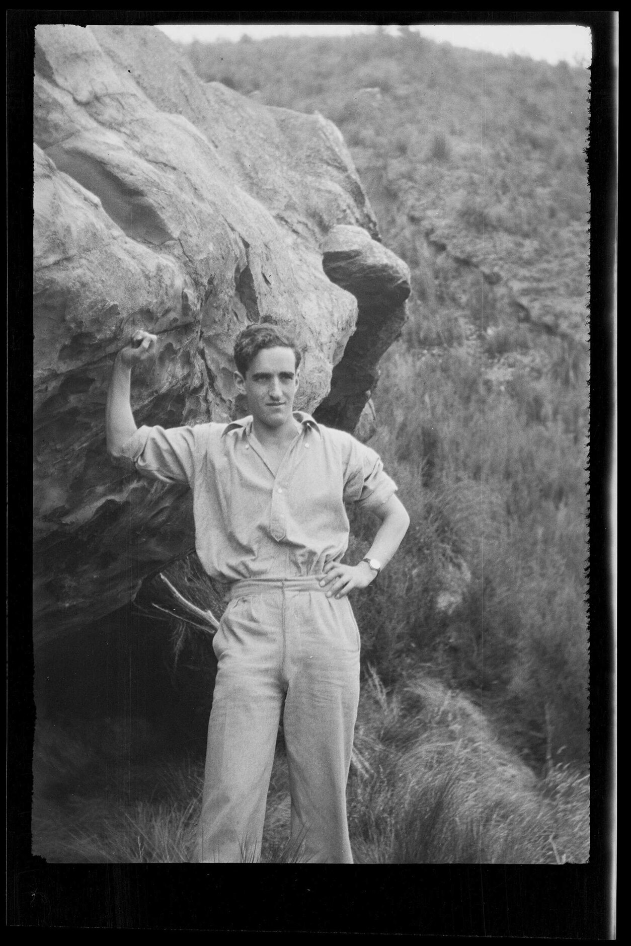 Charles Brasch standing next to a large rock