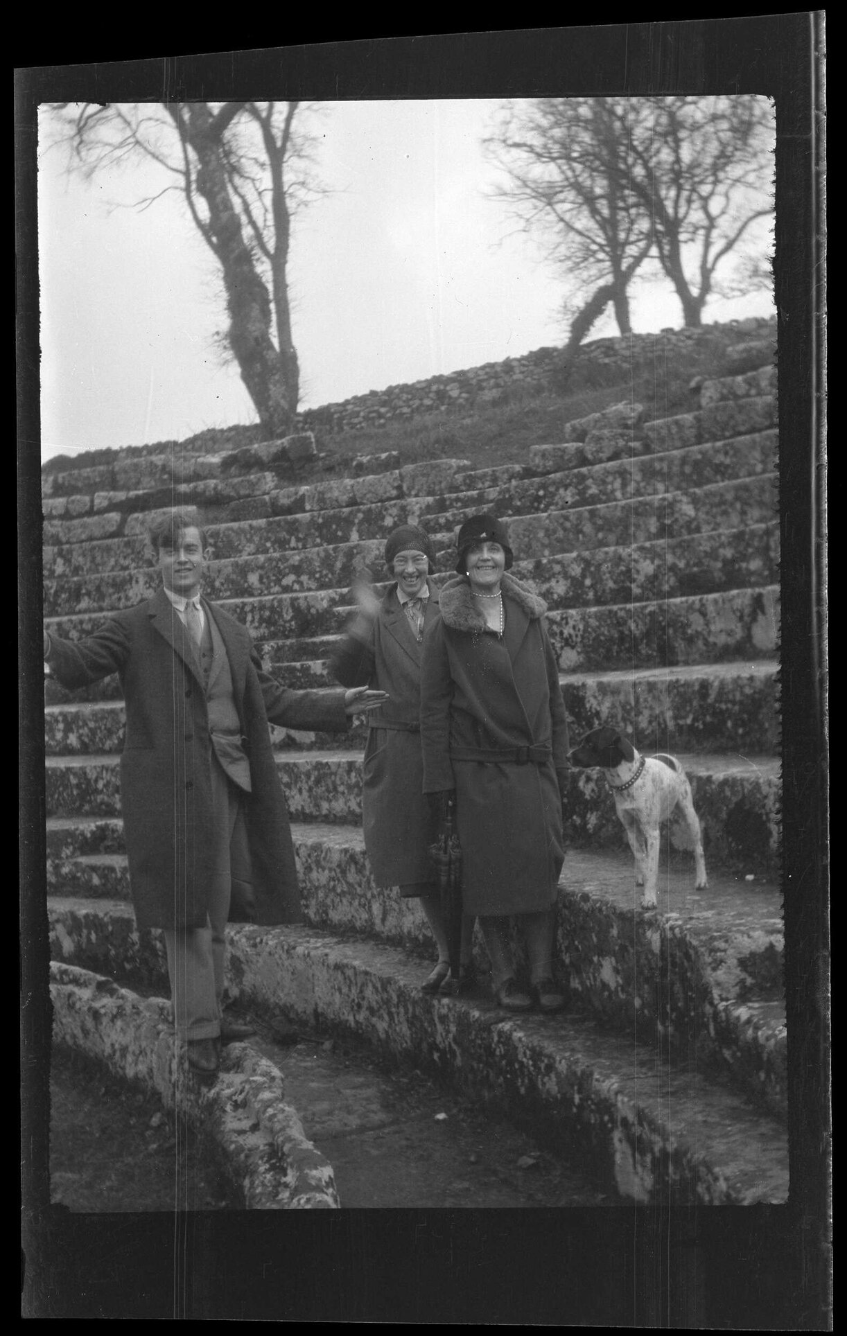 Man and two women with dog, standing on stone steps