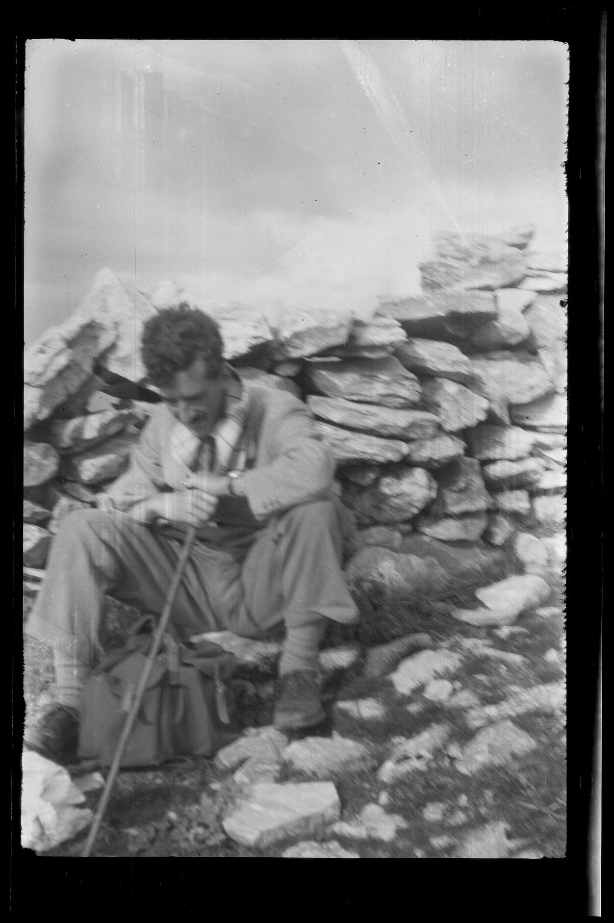 [Charles Brasch] sitting next to rock wall