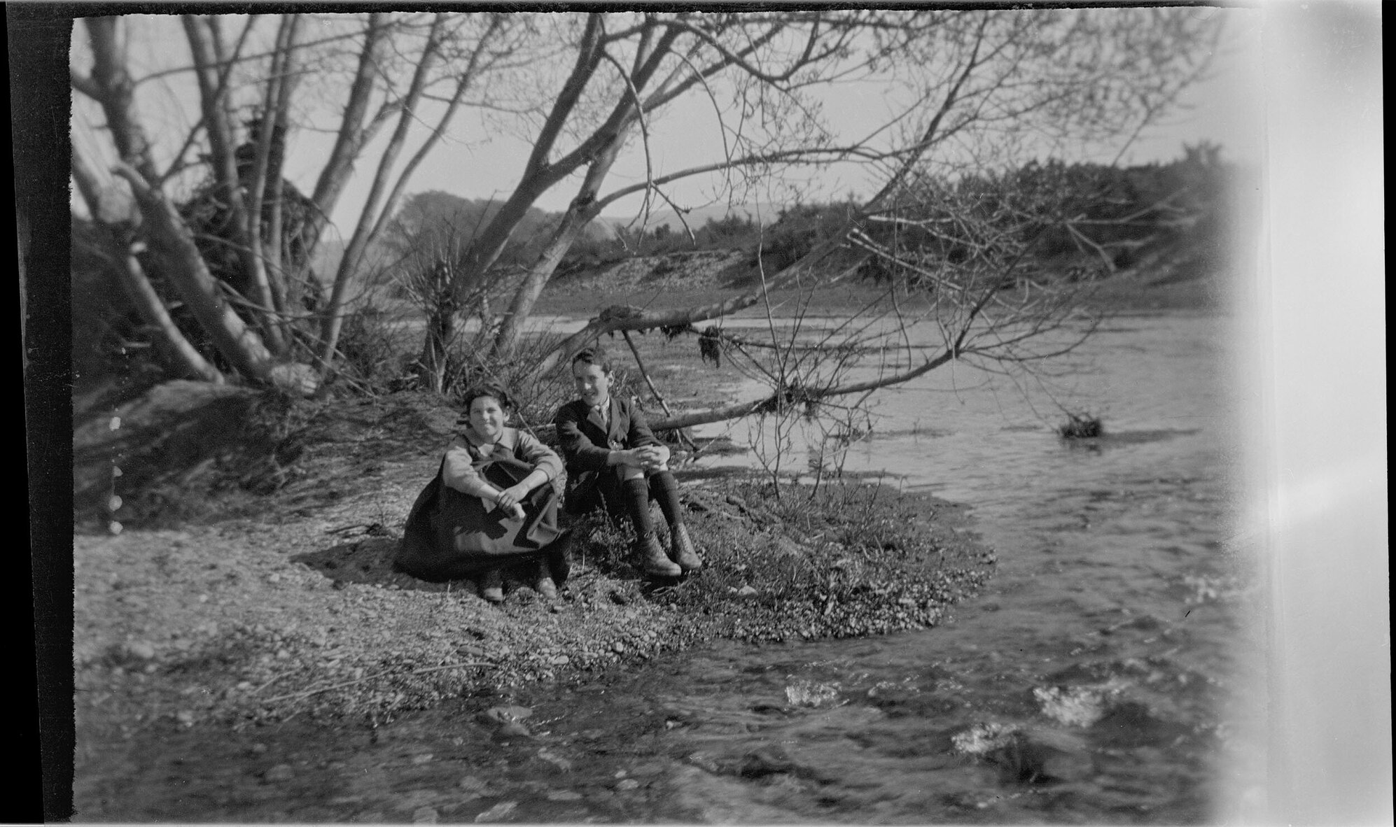 Lesley and Charles Brasch sitting beside a waterway