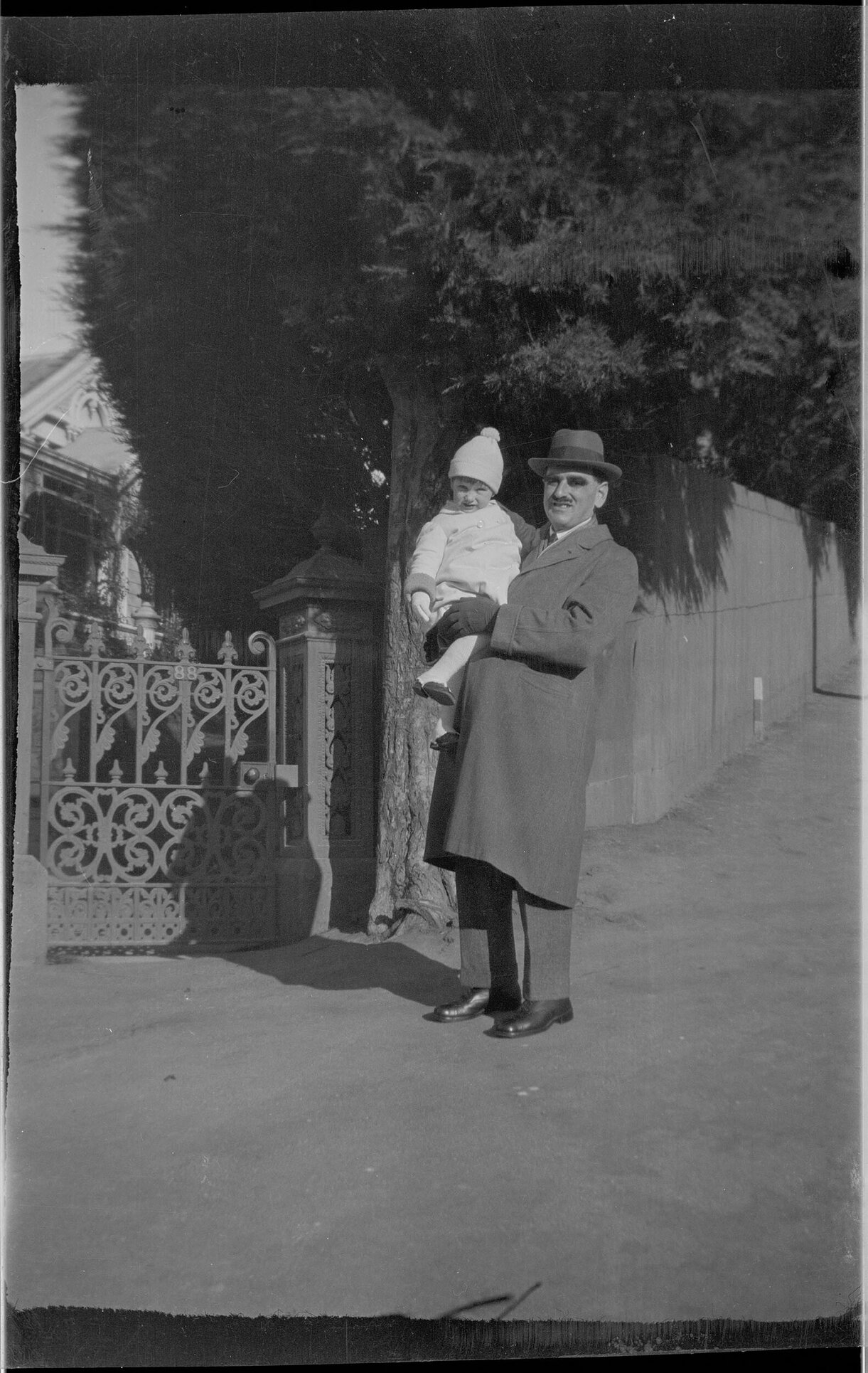 Man holding a child, in front of a gate numbered '88'