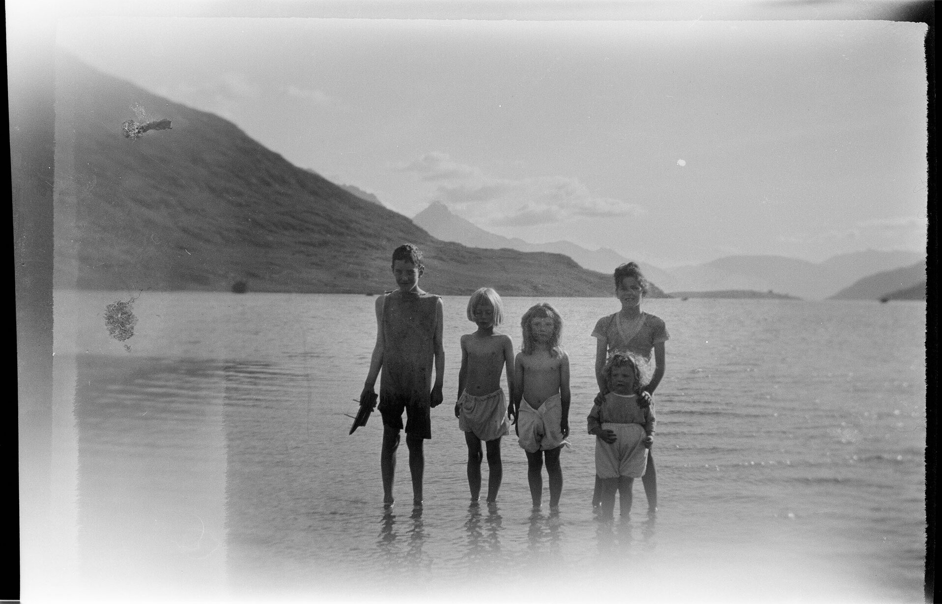 Five children standing in shallow water, with hills and mountains in the background