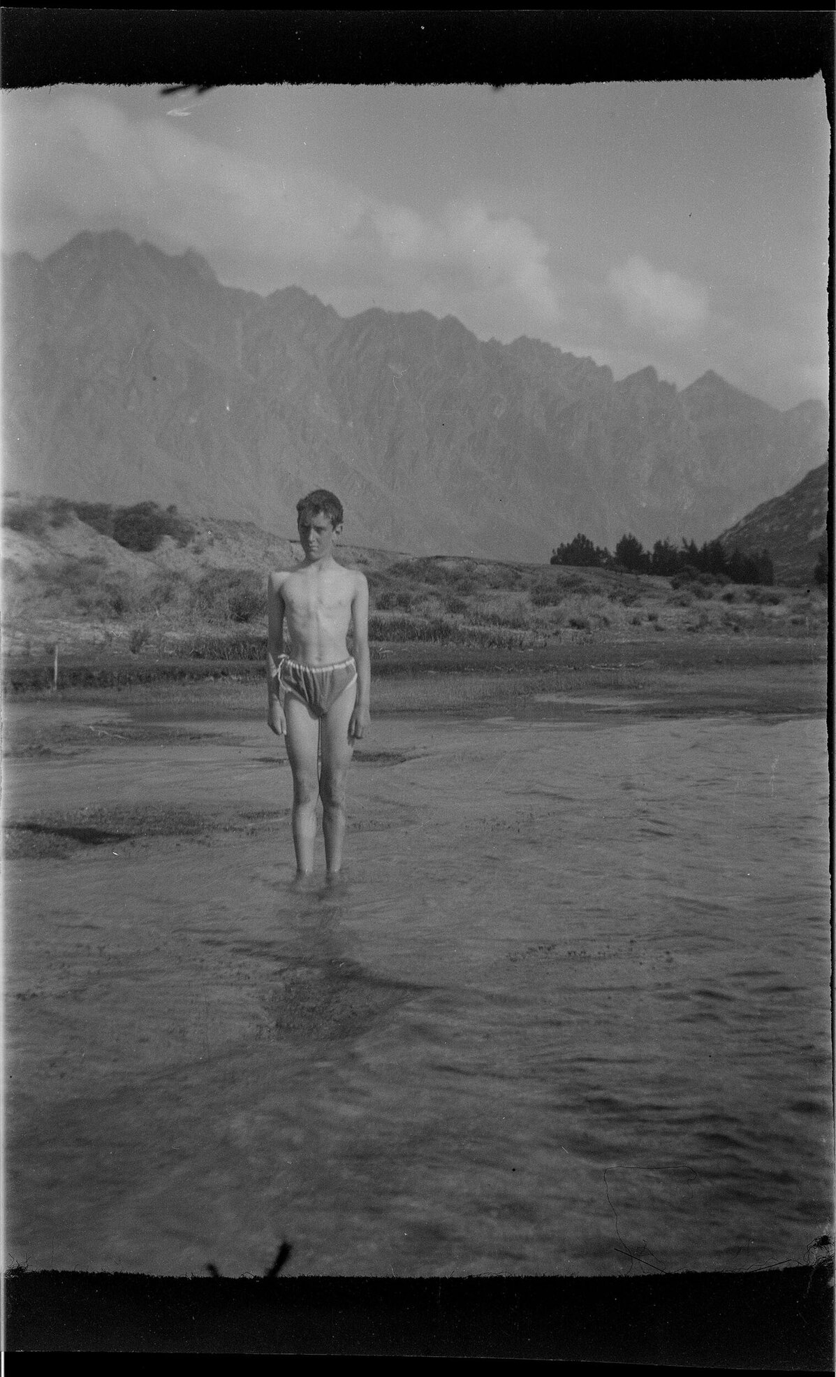 Charles Brasch [?] as a boy, standing in shallow water with mountains in the background
