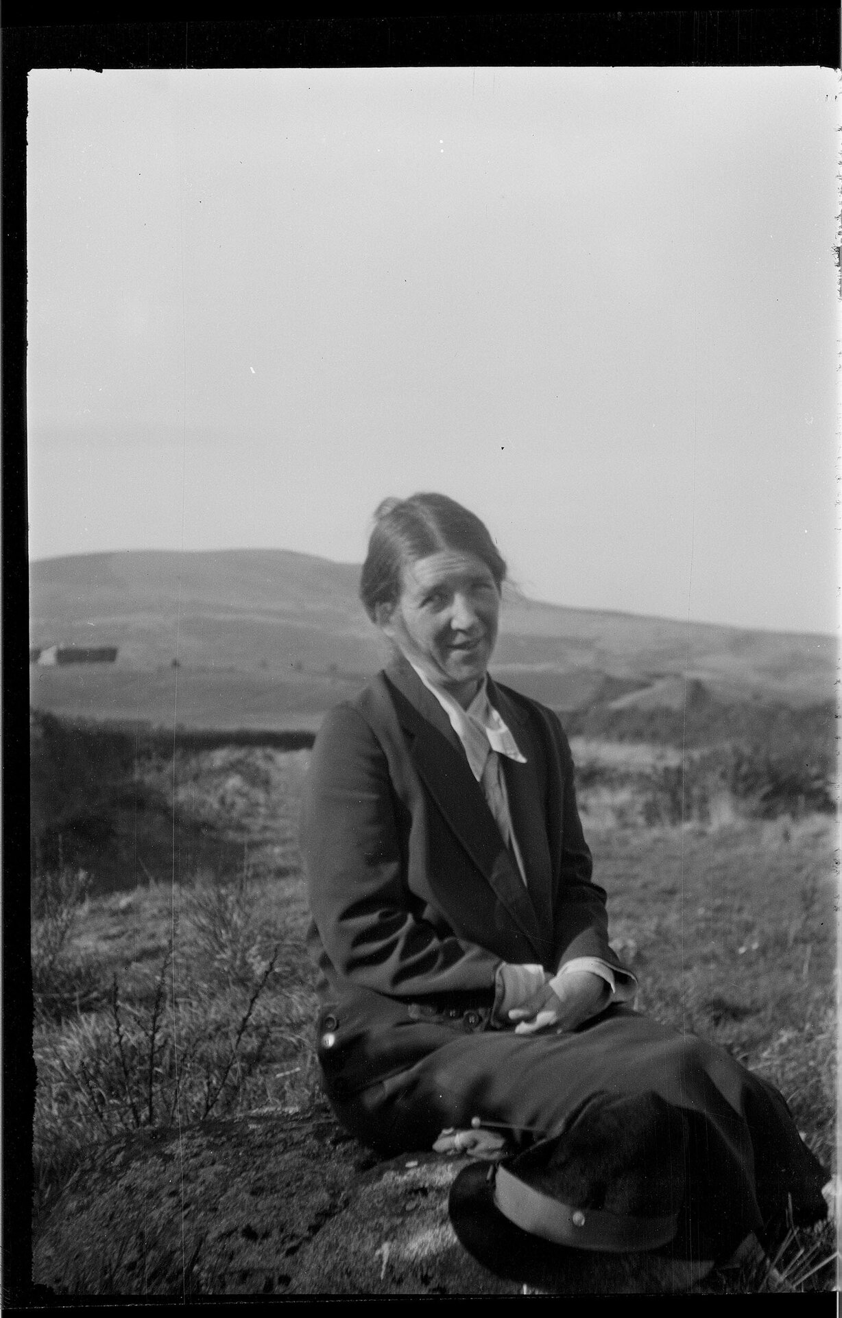 Woman sitting on rock with farmland and hills in background