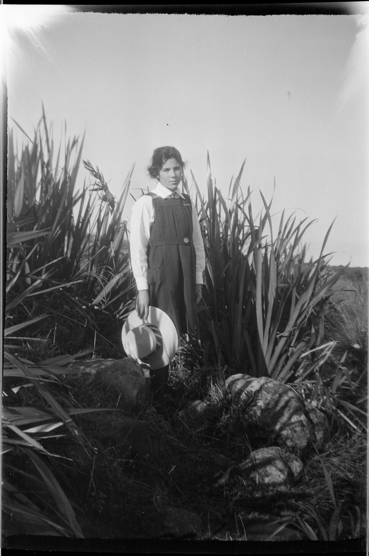 Lesley Brasch [?] standing in front of harakeke and holding a hat