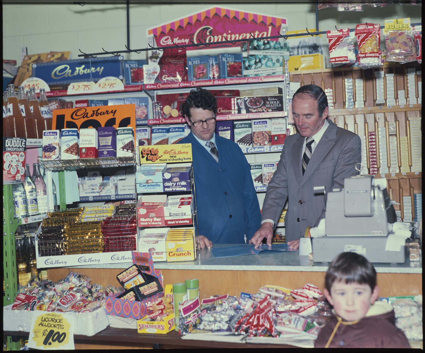 Two men behind shop counter with Cadbury product displays